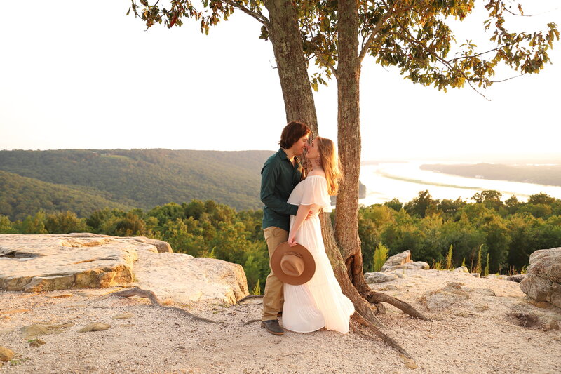 Adventurous couple  kissing under a tree with golden hour light at the top of an overlook in Alabama