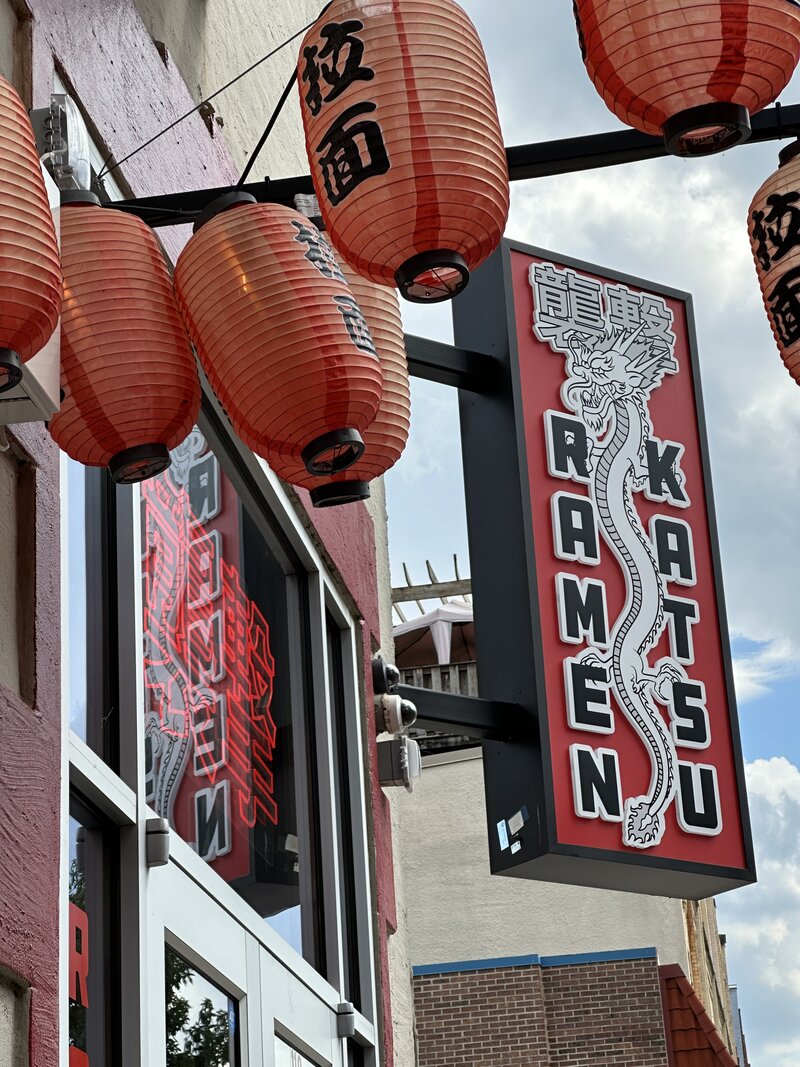 Photo of a ramen shop in Chattanooga, Tennessee, with a graphic red, white, and black sign, red and black lanterns, and reflections of a red neon sign. 