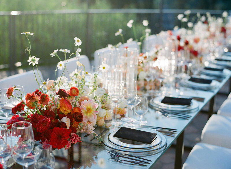 Wedding table design, glass plates with black rims, crystal wine glasses, black menus, and bright red carnations.
