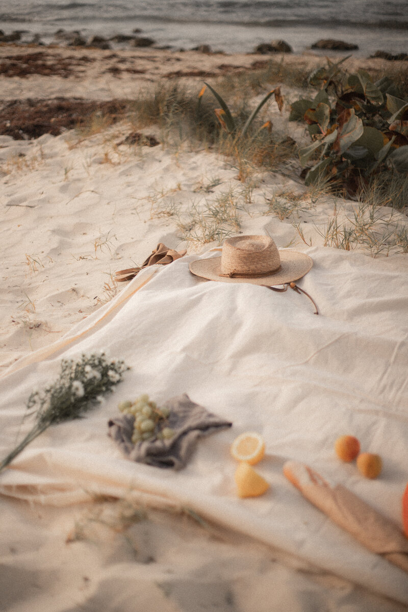 Beach side picnic showing flowers, fruit, and hat