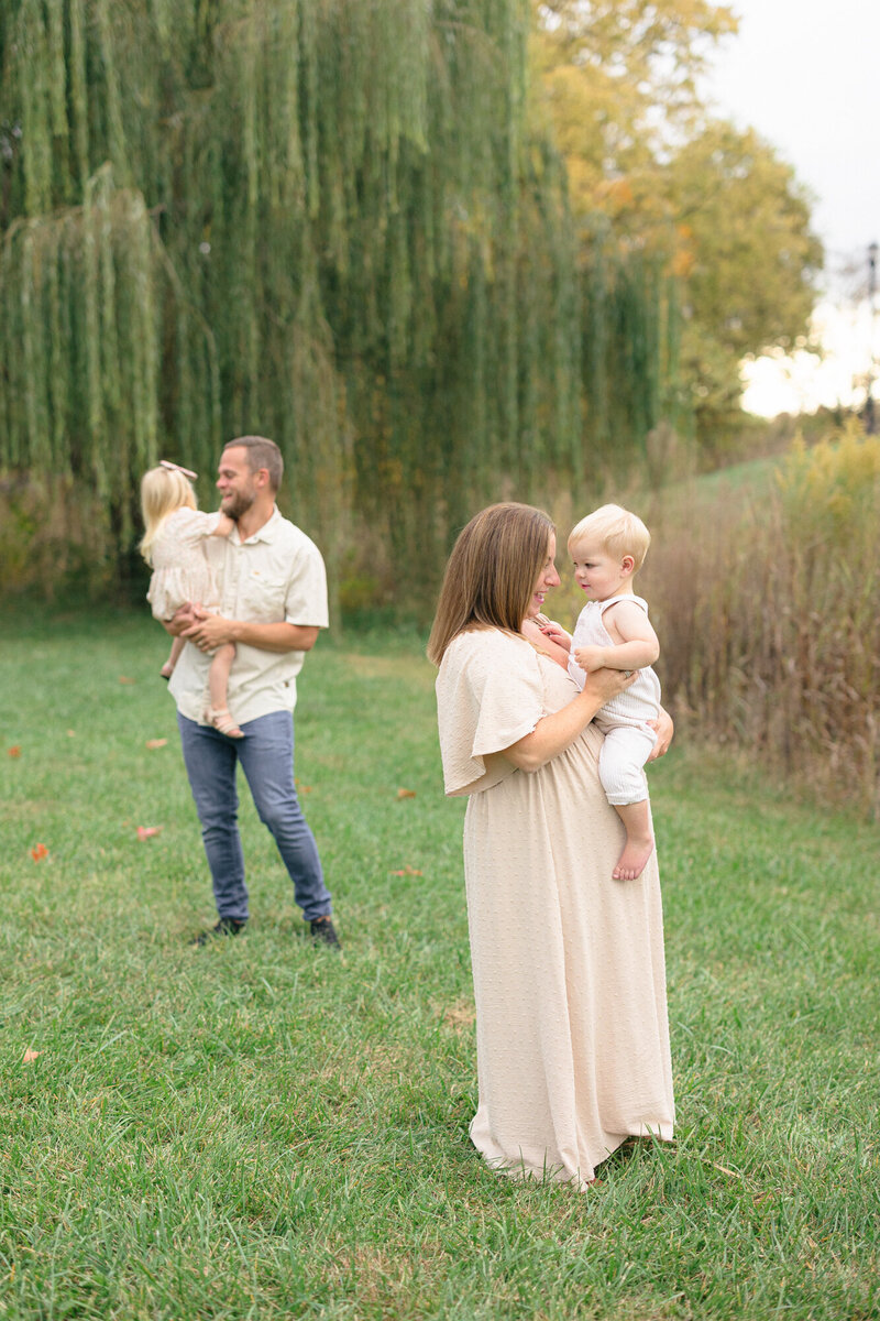 Portrait of a family of four playing in a green park during their louisville maternity photography session