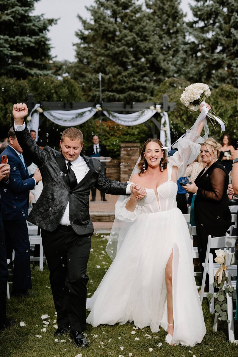 a bride and groom with their arms up cheering as they walking up the aisle