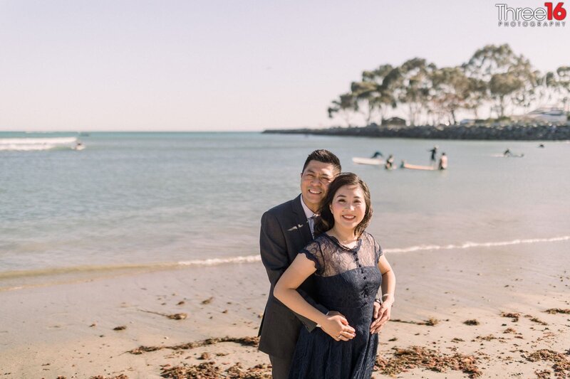 Groom to be holds his fiance from behind while posing for photos on Doheny State Beach