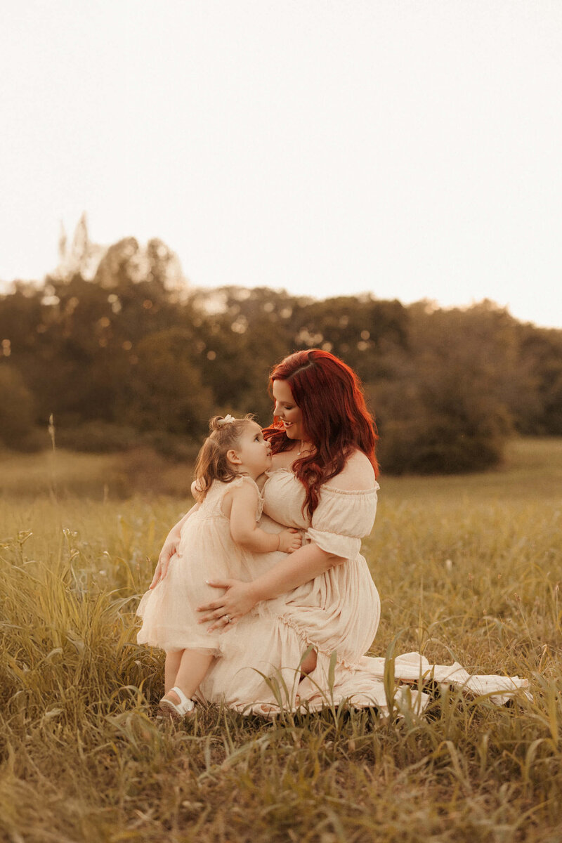 Expecting mother standing in field at sunset, captured in soft, natural light