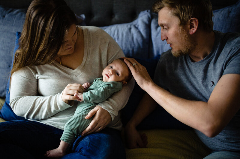 newborn parents gaze at their baby while sitting on their bed.