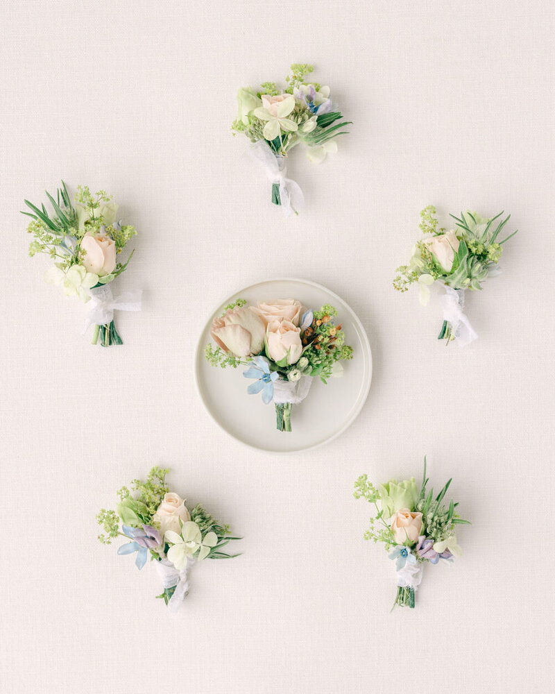 This elegant layflat photograph captures six men's boutonnieres beautifully arranged during the groom's getting ready photos. The attention to detail and sophisticated presentation reflect the luxury and style of the wedding day.