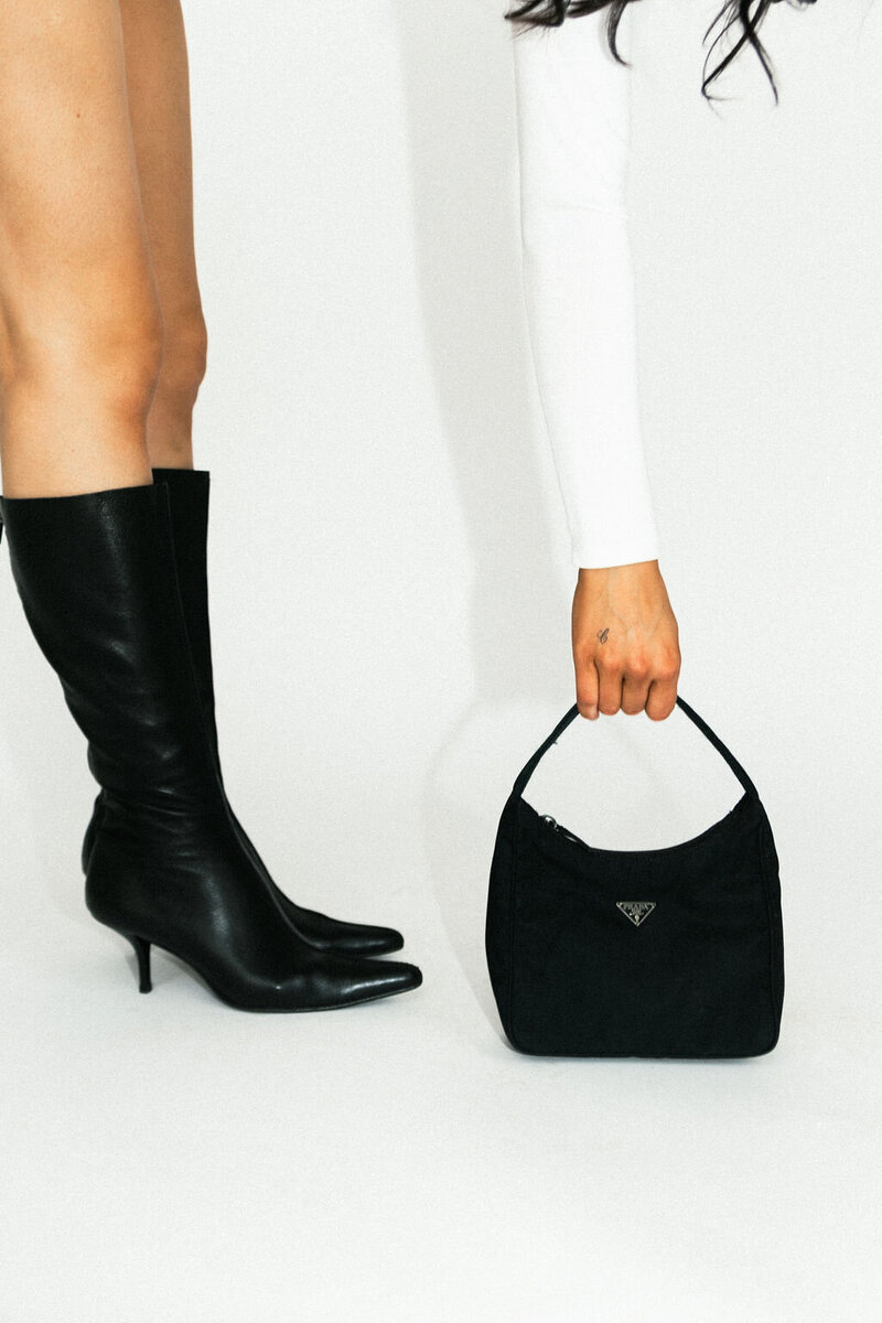 A pair of sleek black boots and a hand holding a designer bag