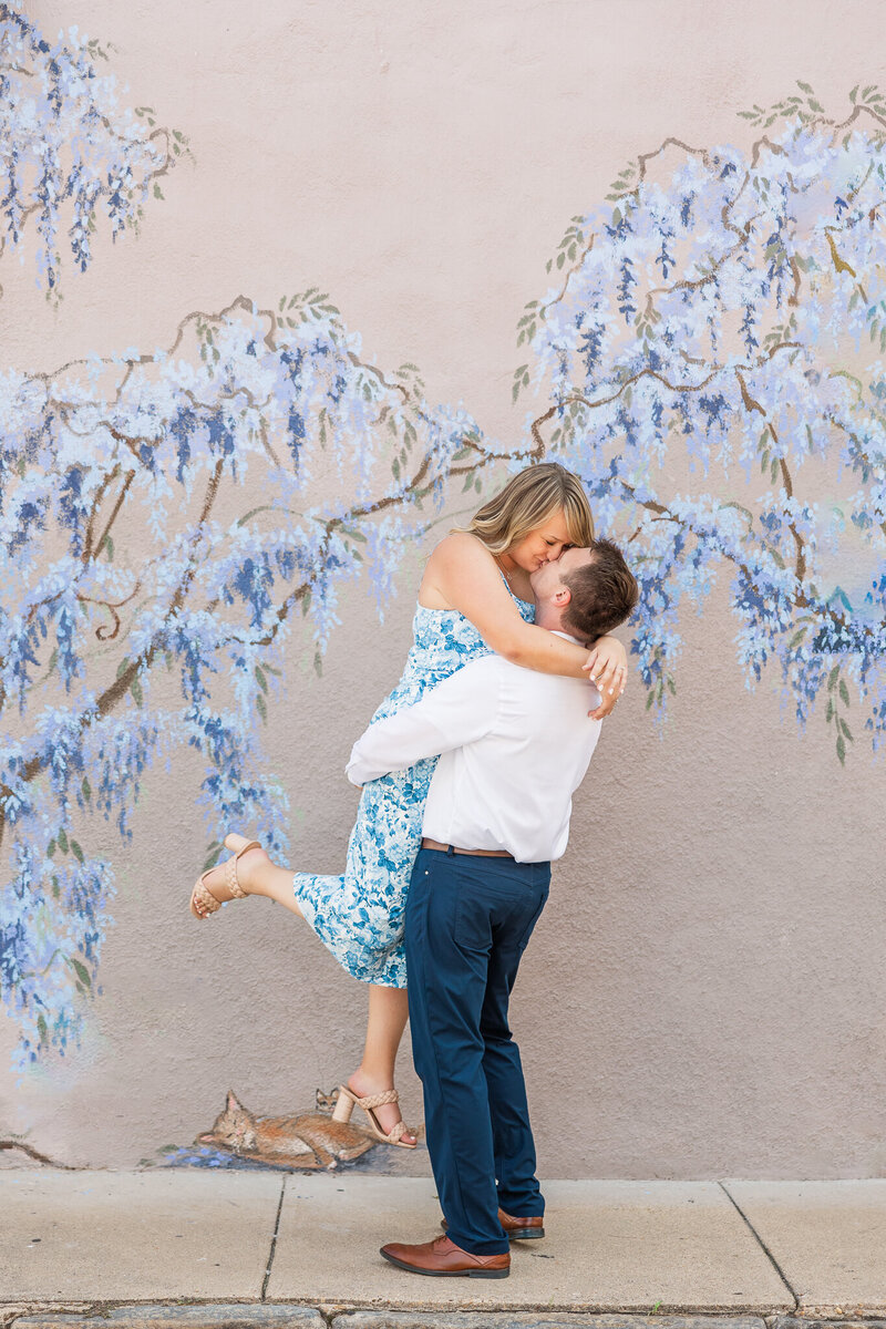 a couple kisses in front of a blue flower mural