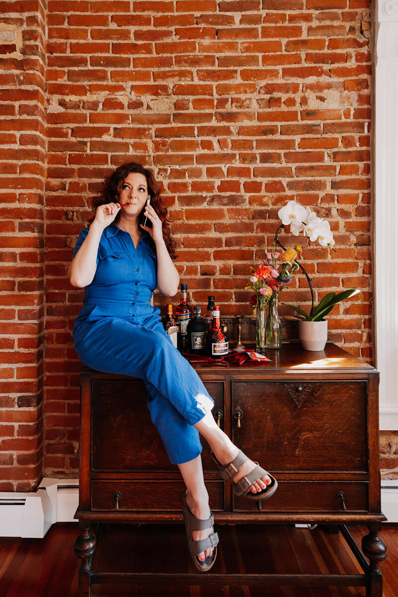 A woman sitting on a dresser talking on the phone.