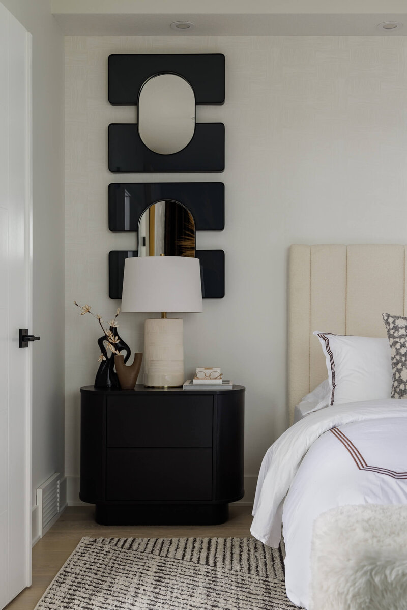 Primary bedroom with oval dark nightstand, table lamp and accent mirrors. 