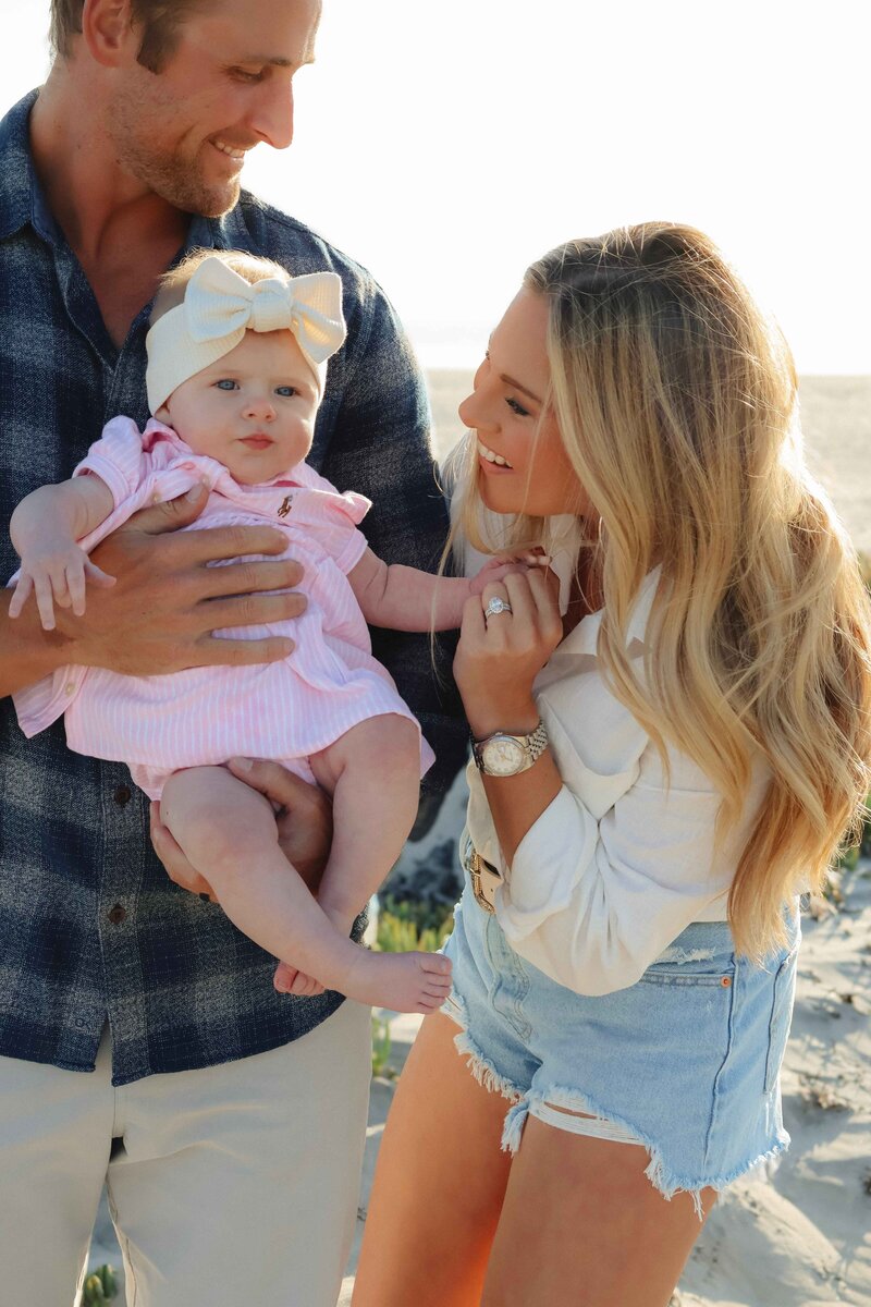 A family smiles together for a photo on the beach, captured by a family photographer.