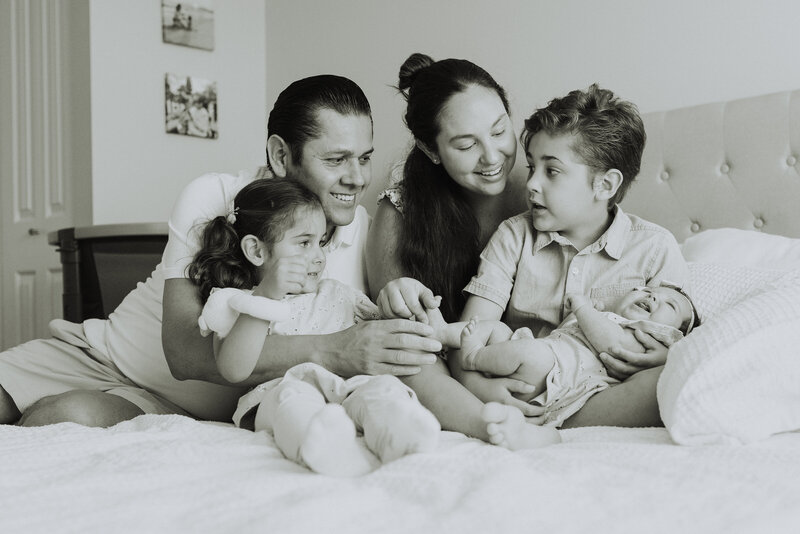 black and white photo of a family sitting on the bed while the little boy holds the new baby taken by a langley photographer