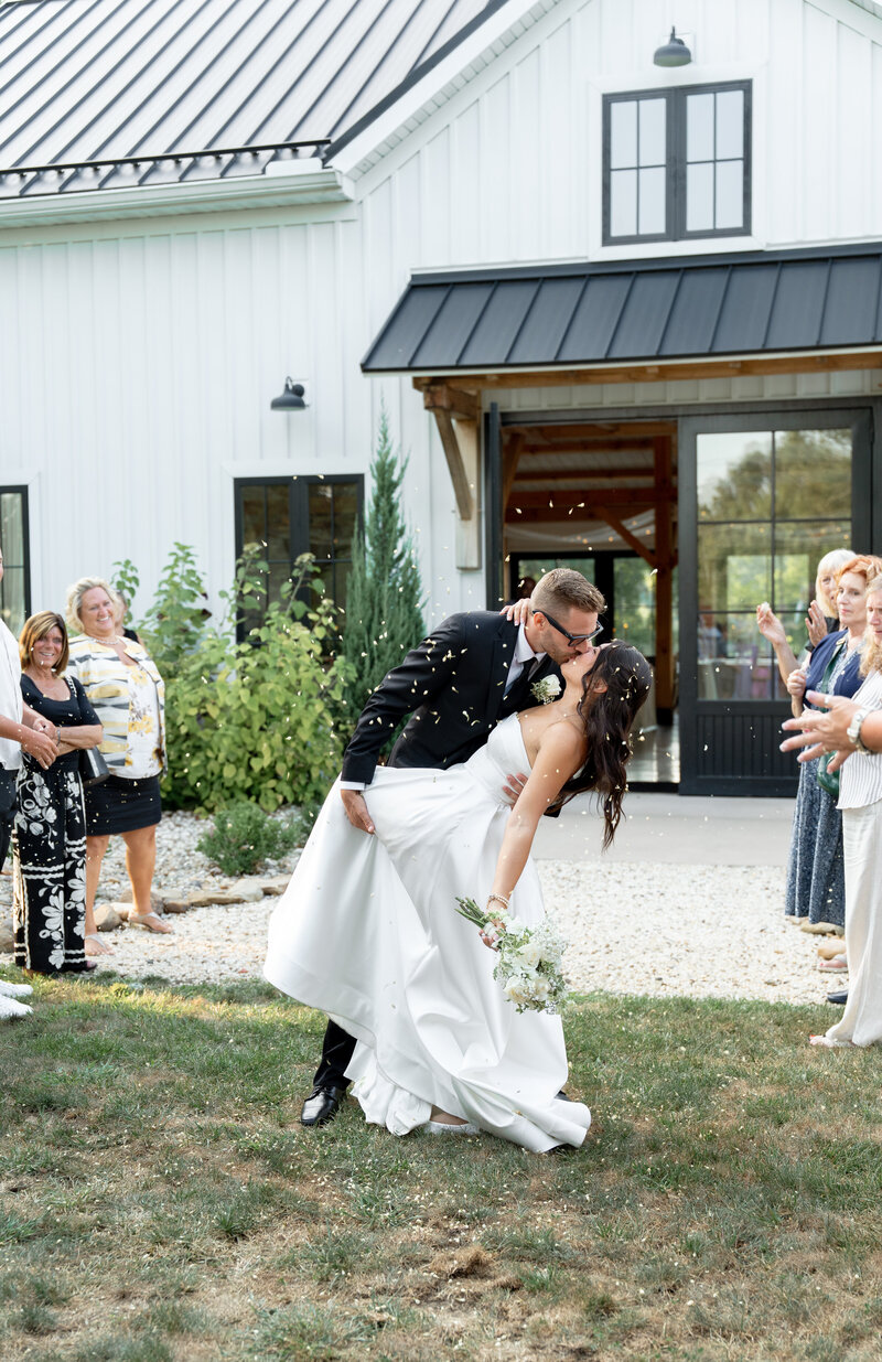 A newly married couple exiting the ceremony. They are happy and smiling at each other. White flower petals fall around them 