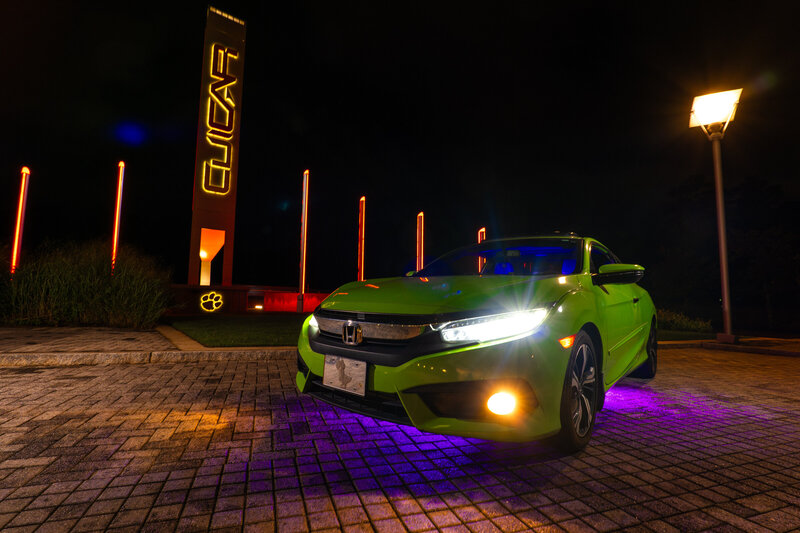 A green car parked outside at night with a purple under glow 