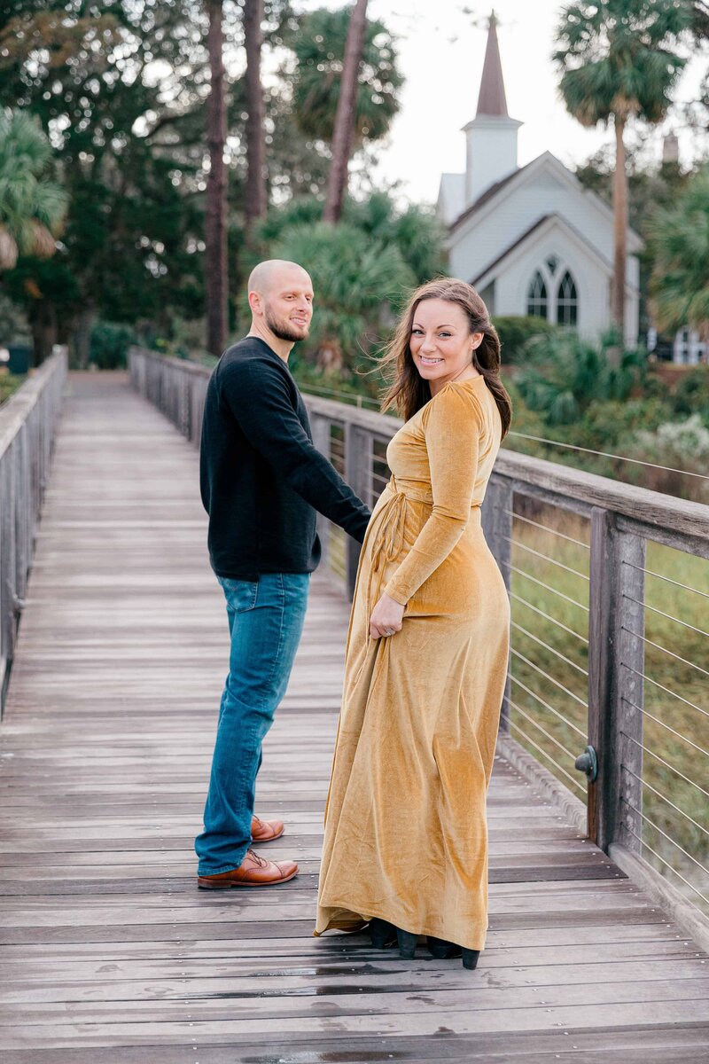 Man holding wife's hand as they walk on dock for maternity portrait session with Palmetto Bluff Photographer Lamp and Light Photography.