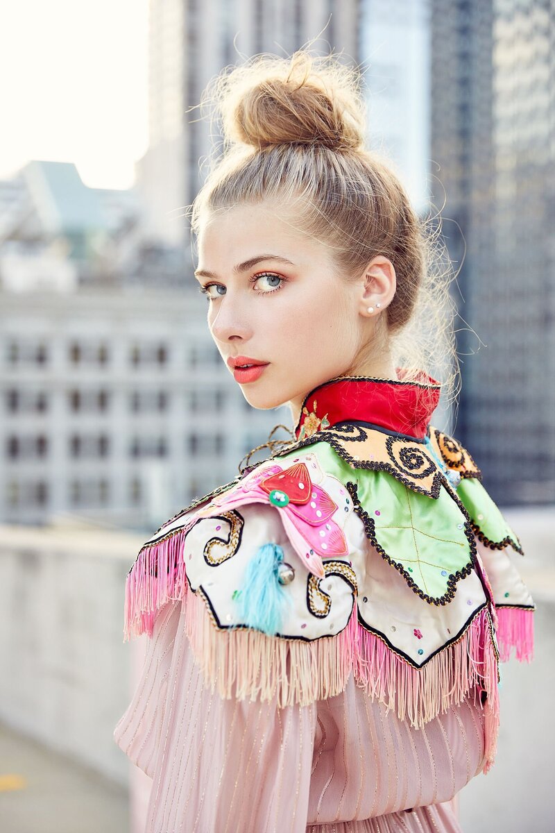Fashion-forward model in a vibrant, embellished cape with fringe detail, looking over her shoulder on a rooftop in Chicago during a photography workshop with Tara Rochelle.

