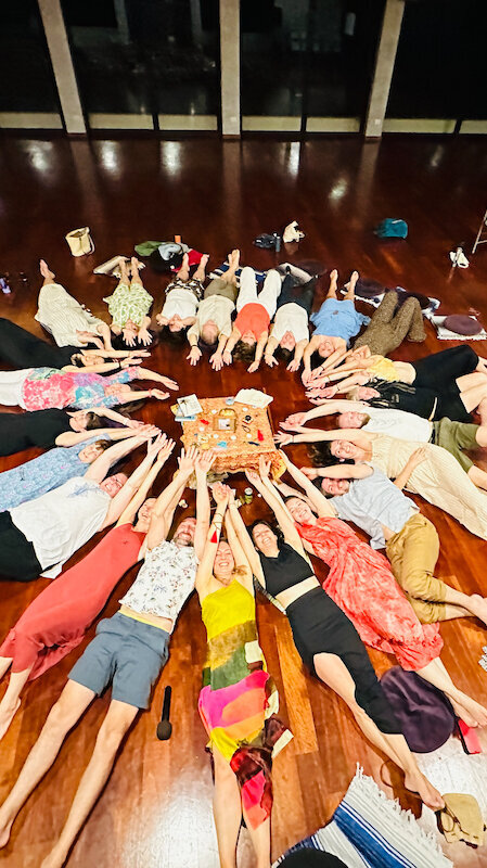 Ground of people lying on the ground in a circle with hands reaching towards the center Psychologist Leadership Coach