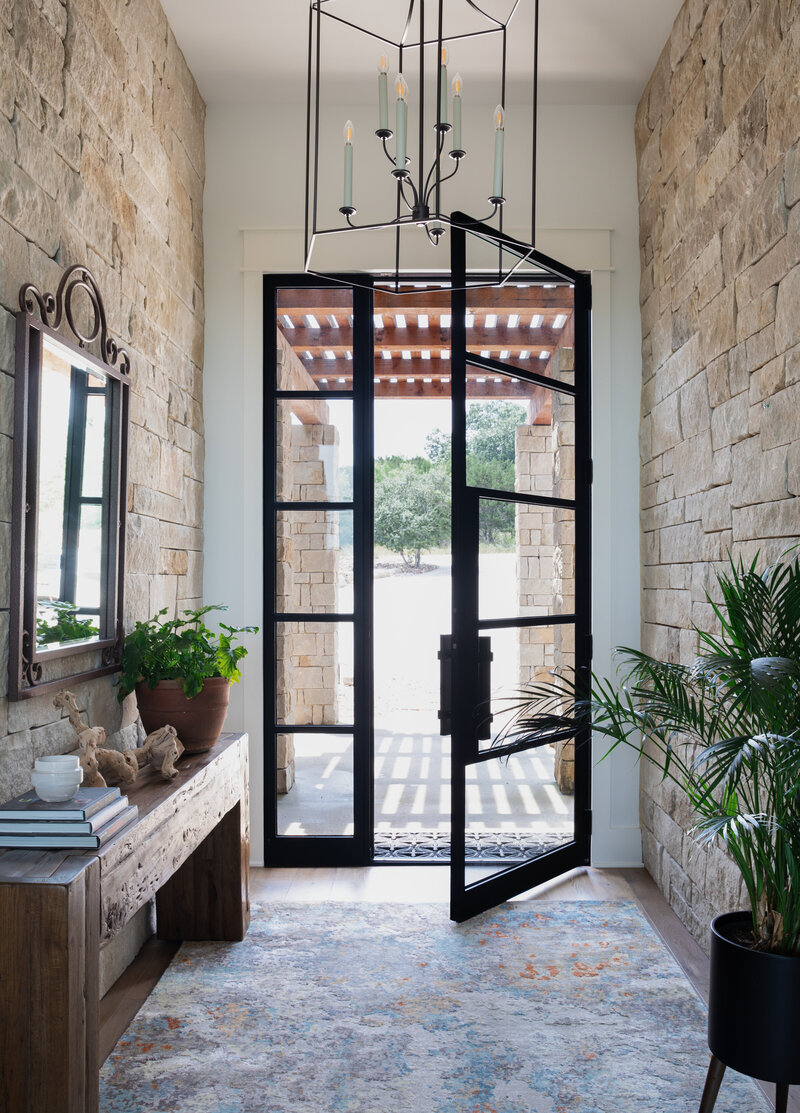 Large entryway/foyer with black steel door, dry stacked stone walls, large candelabra chandelier and earth tones rug