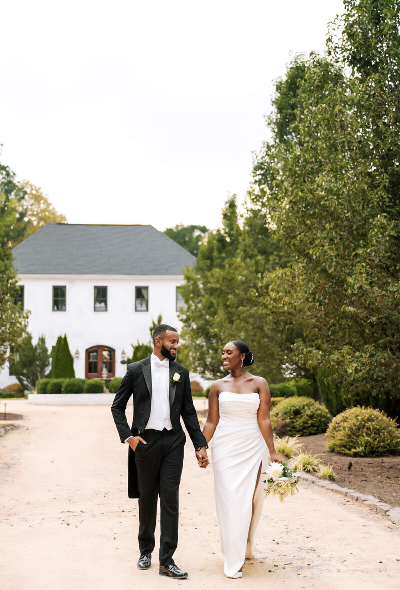 bride and groom smiling in front of The Bradford wedding venue in New Hill, North Carolina