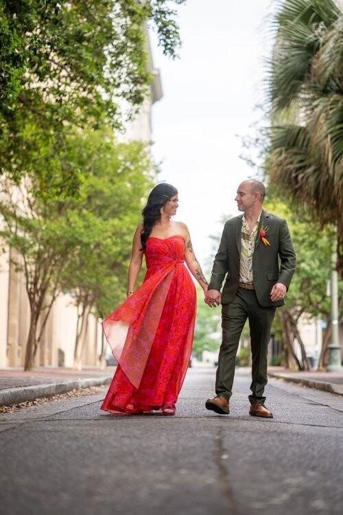 Bride in a red dress walks through downtown NOLA with groom in a green suit on their wedding day
