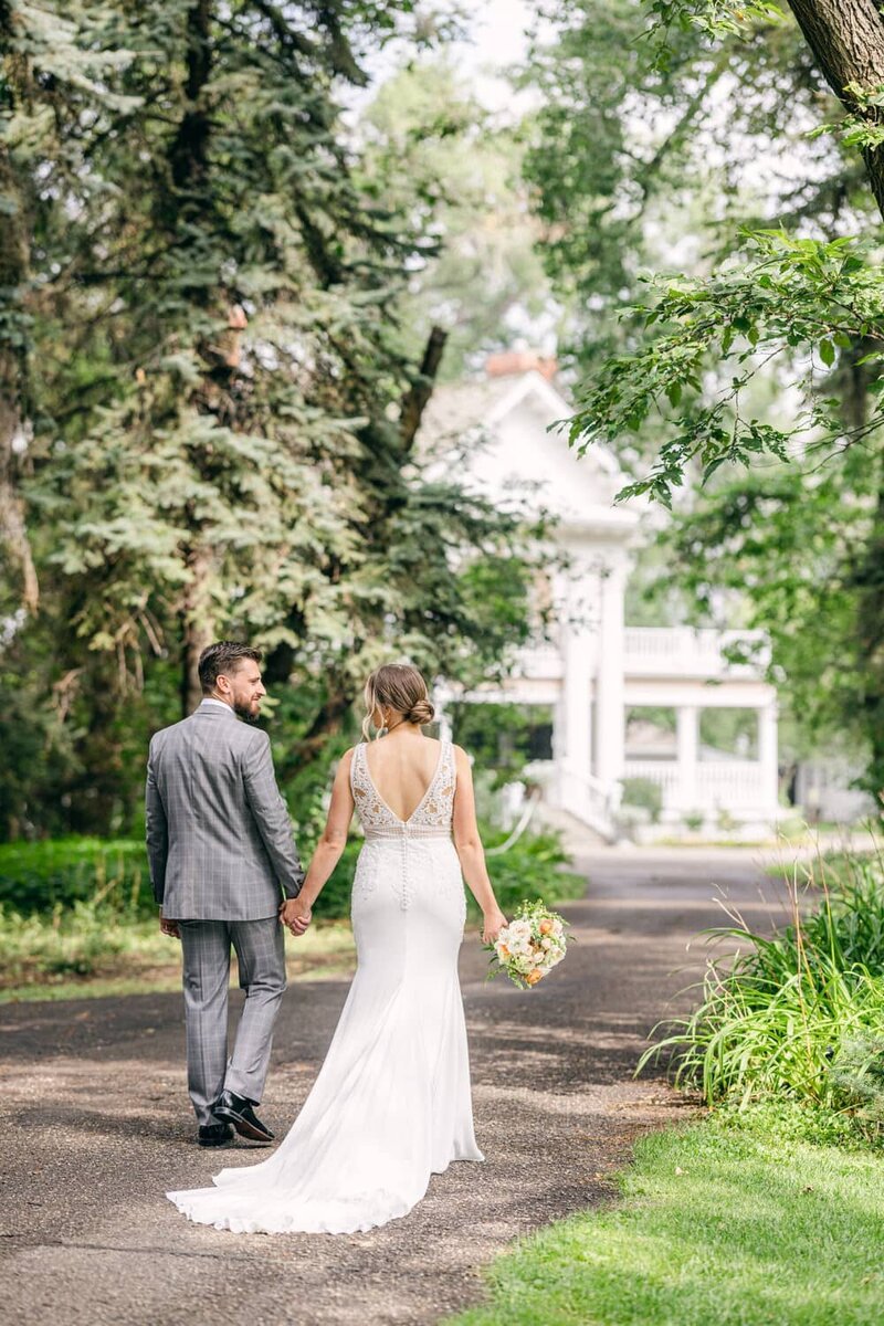 This charming image captures the bride and groom walking hand in hand along the road leading to the main building at Norland Estate in Lethbridge. The estate’s elegant backdrop and the couple’s joyful connection create a timeless and romantic moment.