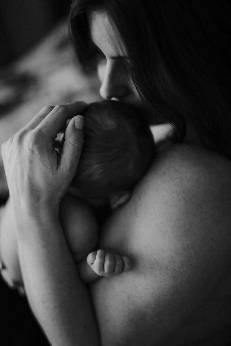 En mamma håller sitt nyfödda barn i sin famn och luktar på huvudet under en nyföddfotografering i Göteborg