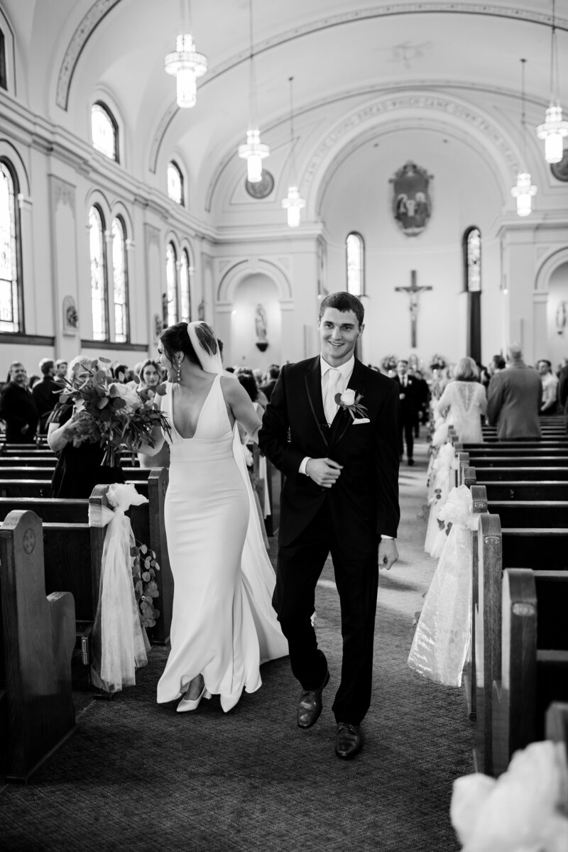 Bride and groom joyfully stroll up the church aisle, greeting guests along the way, as husband and wife.