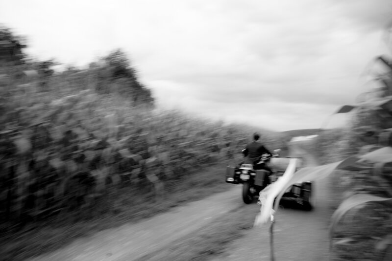 black and white photo of bride and groom riding away on a motorcycle