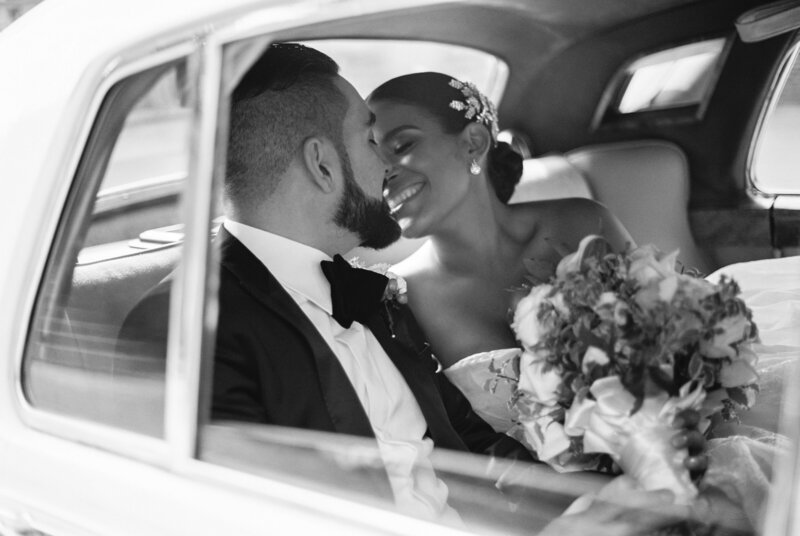 Bride and groom sharing an intimate moment inside a vintage car after their wedding ceremony at Oxon Hill Manor, Maryland — classic black and white portrait captured by Asia Pimentel Photography.