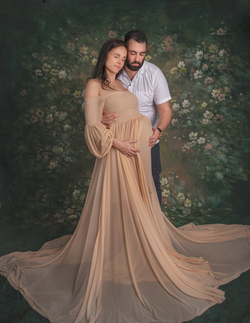 Pregnant couple sharing an intimate moment, with mom lying in a stunning gown and dad by her side, captured in a classic maternity photography session in Ottawa."