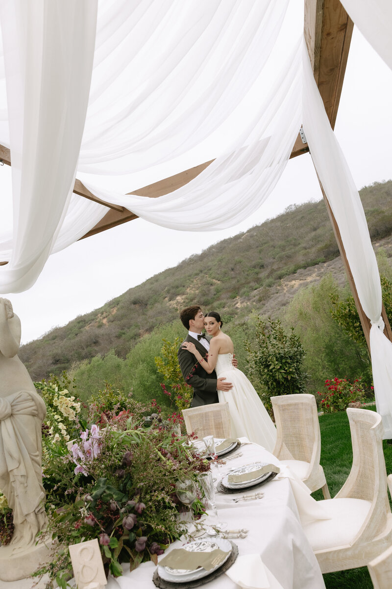 Northern California Wedding Photographer capturing a couple’s intimate embrace beneath flowing white drapery at their outdoor reception
