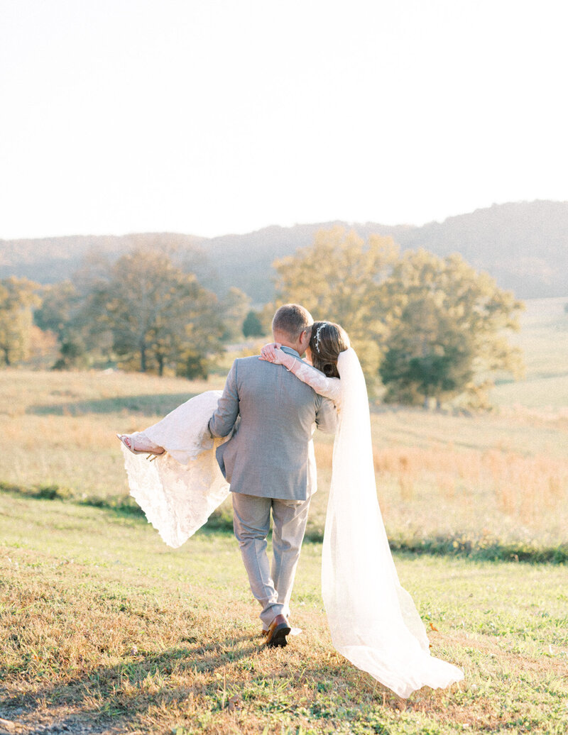 A groom carries his bride away from the camera toward a beautiful fall landscape by Chattanooga wedding photographer, Kelsey Dawn Photography