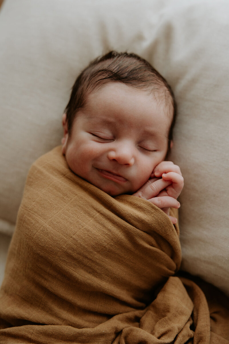 Newborn baby wrapped in orange wrap smiles while sleeping at melbourne newborn photography session by Natalie Hughes Photography