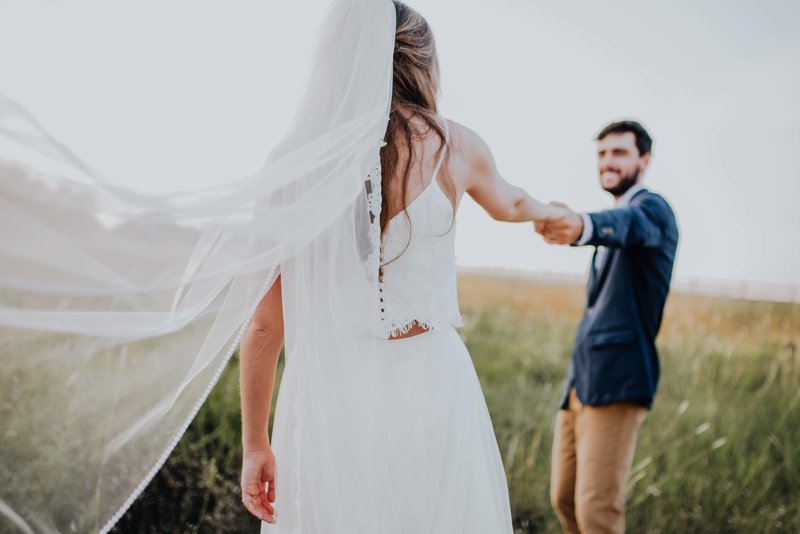 Groom holding hand of bride, smiling at her and leading her off into the sunset.