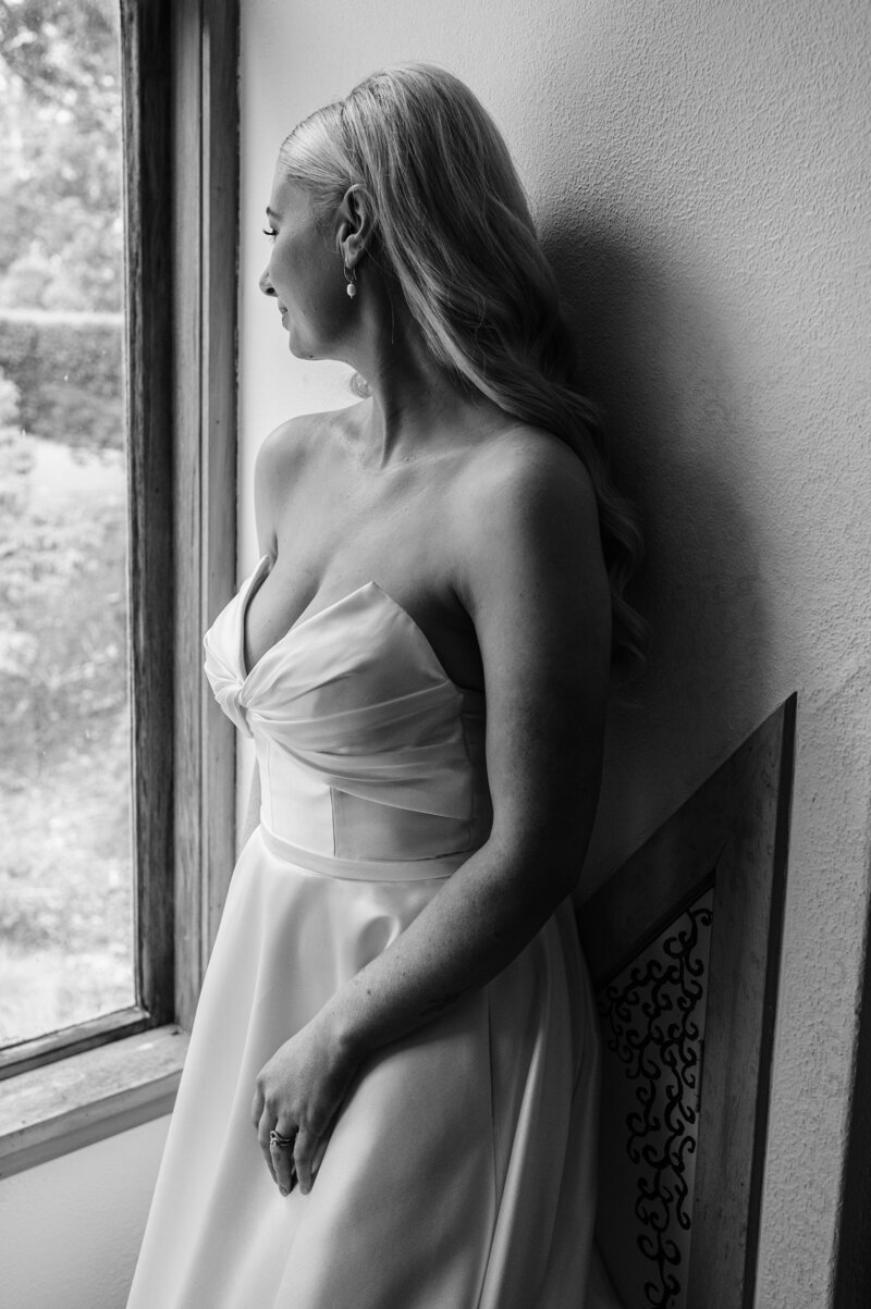 black and white photo of bride in paperswan wedding dress looking out of a window in gore