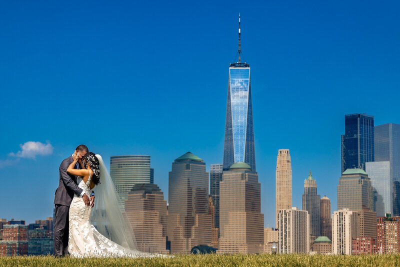 The bride and groom share a romantic embrace with the iconic Manhattan skyline and One World Trade Center towering behind them.