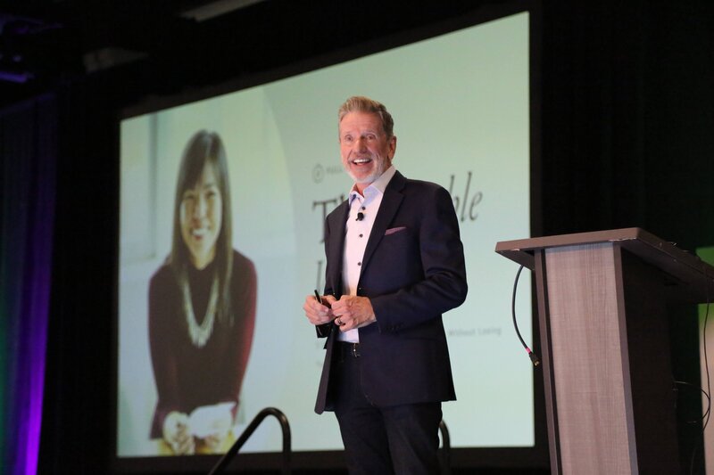 Michael Hyatt on a dimly lit stage addressing an audience, spotlight shining down behind him.