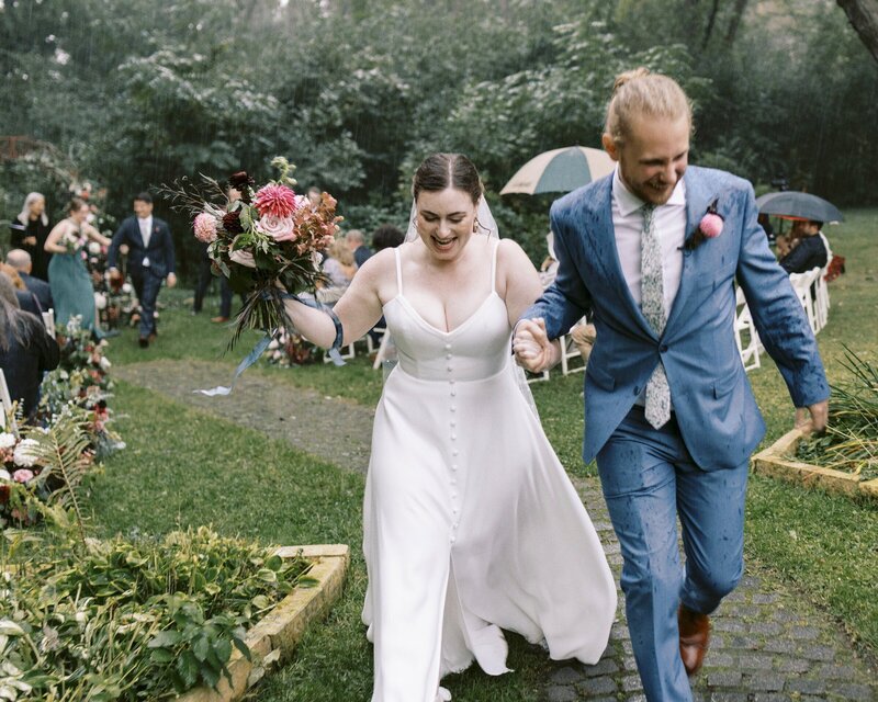 bride and groom on their wedding day holding hands running in the rain with bouquet in other hand by wedding photographers in minnesota tom thornton photography