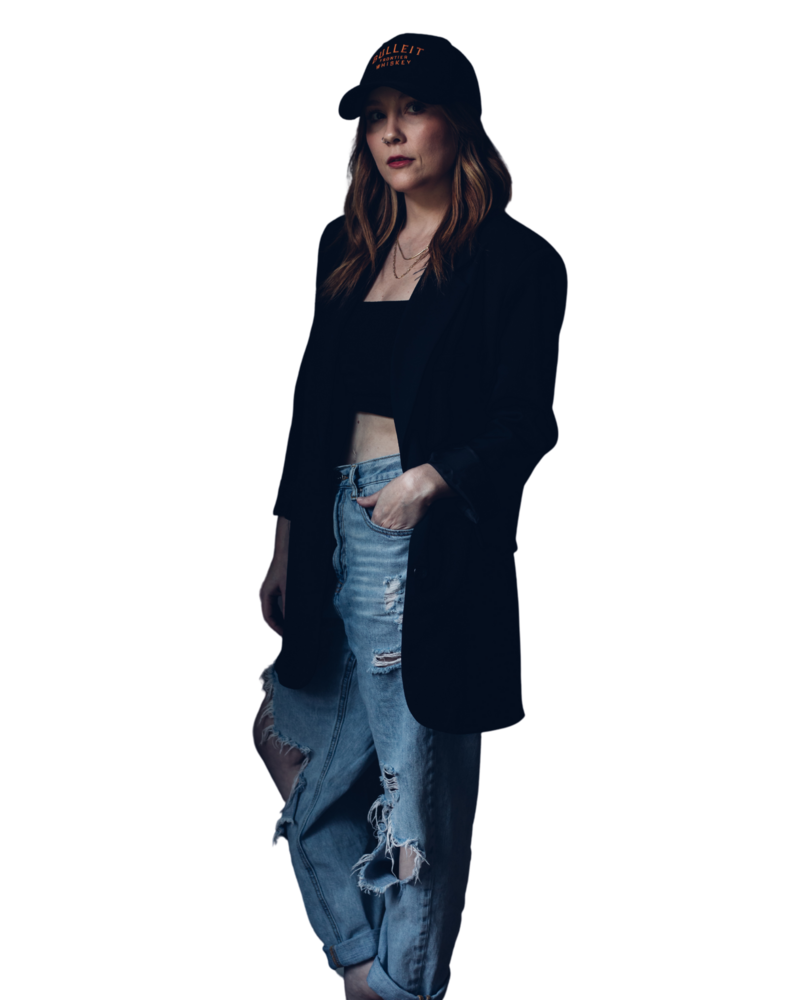 A woman wears a black hat, black blazer, black crop top, and ripped blue jeans, posing with one hand in her pocket against a dark background as the owner of a company providing branding and web design for female entrepreneurs.