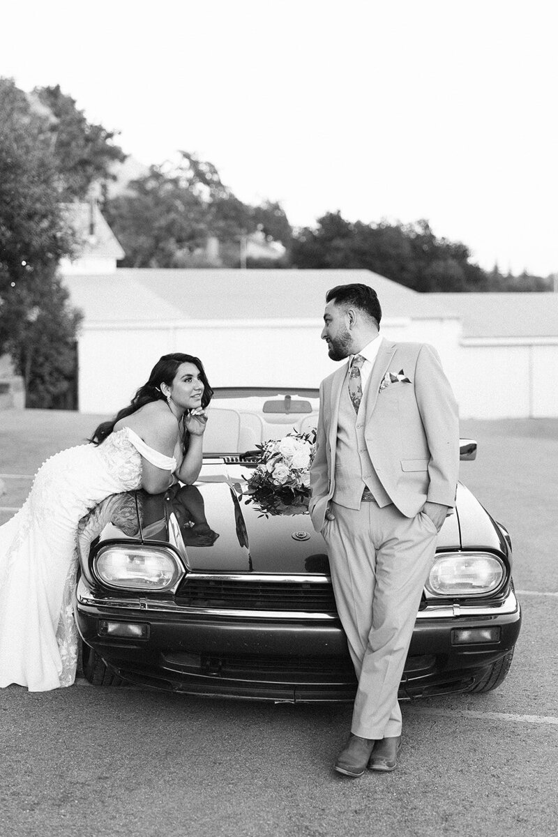 Black and white photo Bride and Groom leaning on a vintage jaguar  while looking at each over