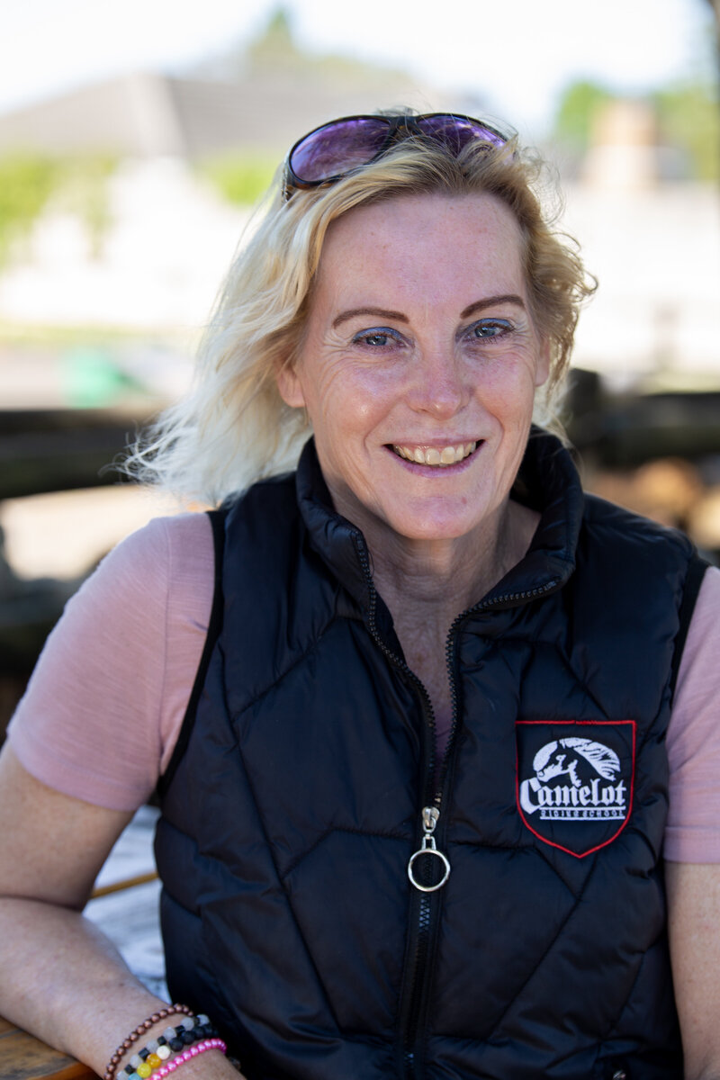 Adele Blignaut, instructor at Camelot Horse Riding School, smiling while wearing a Camelot-branded vest.