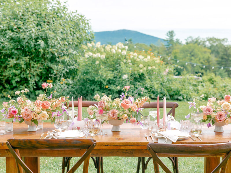 Wedding reception table with wood chairs with pink candles and floral centerpieces in front of a blooming landscape