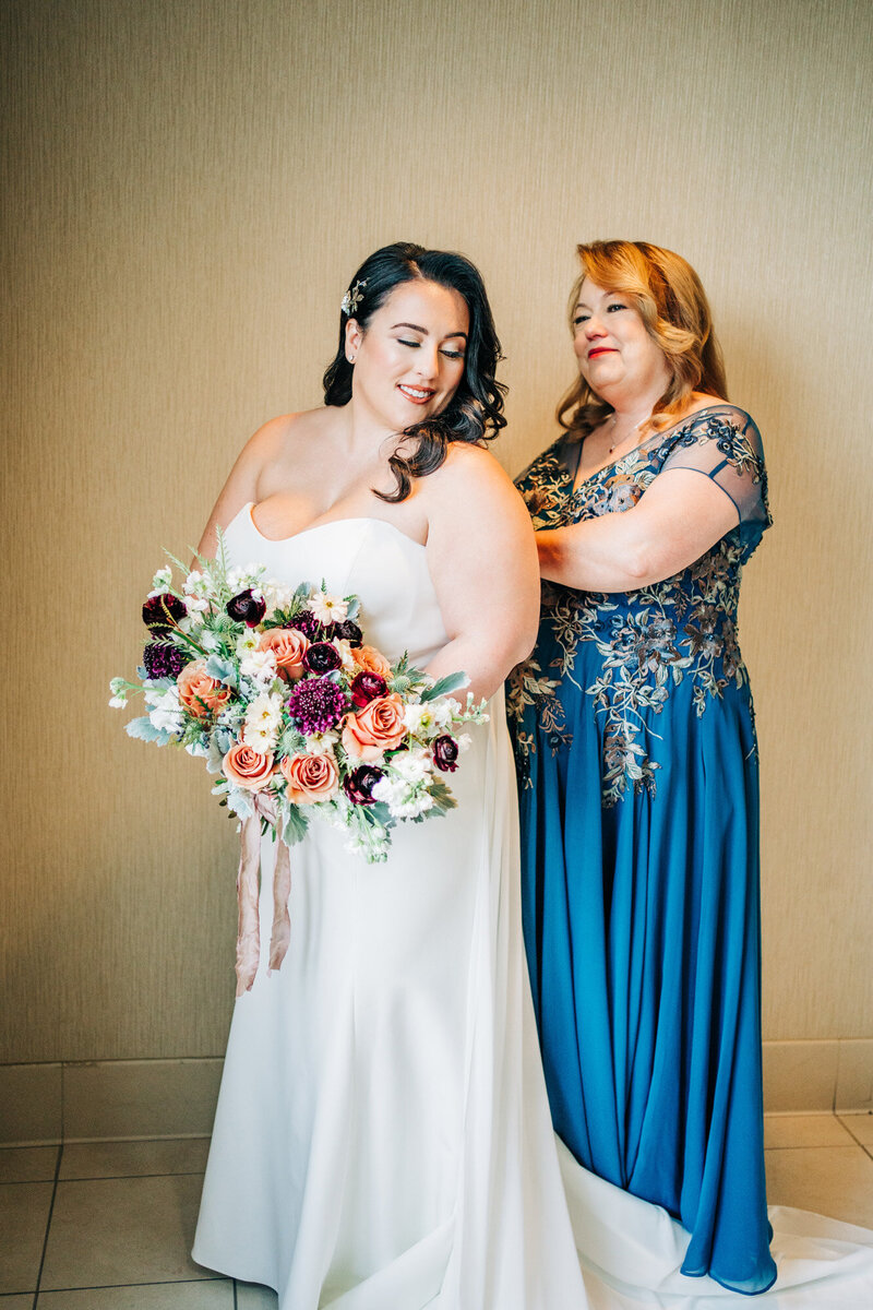Bride holding her bouquet while her mother is fixing her wedding dress altered by Bridal Alterations by Kirstyn