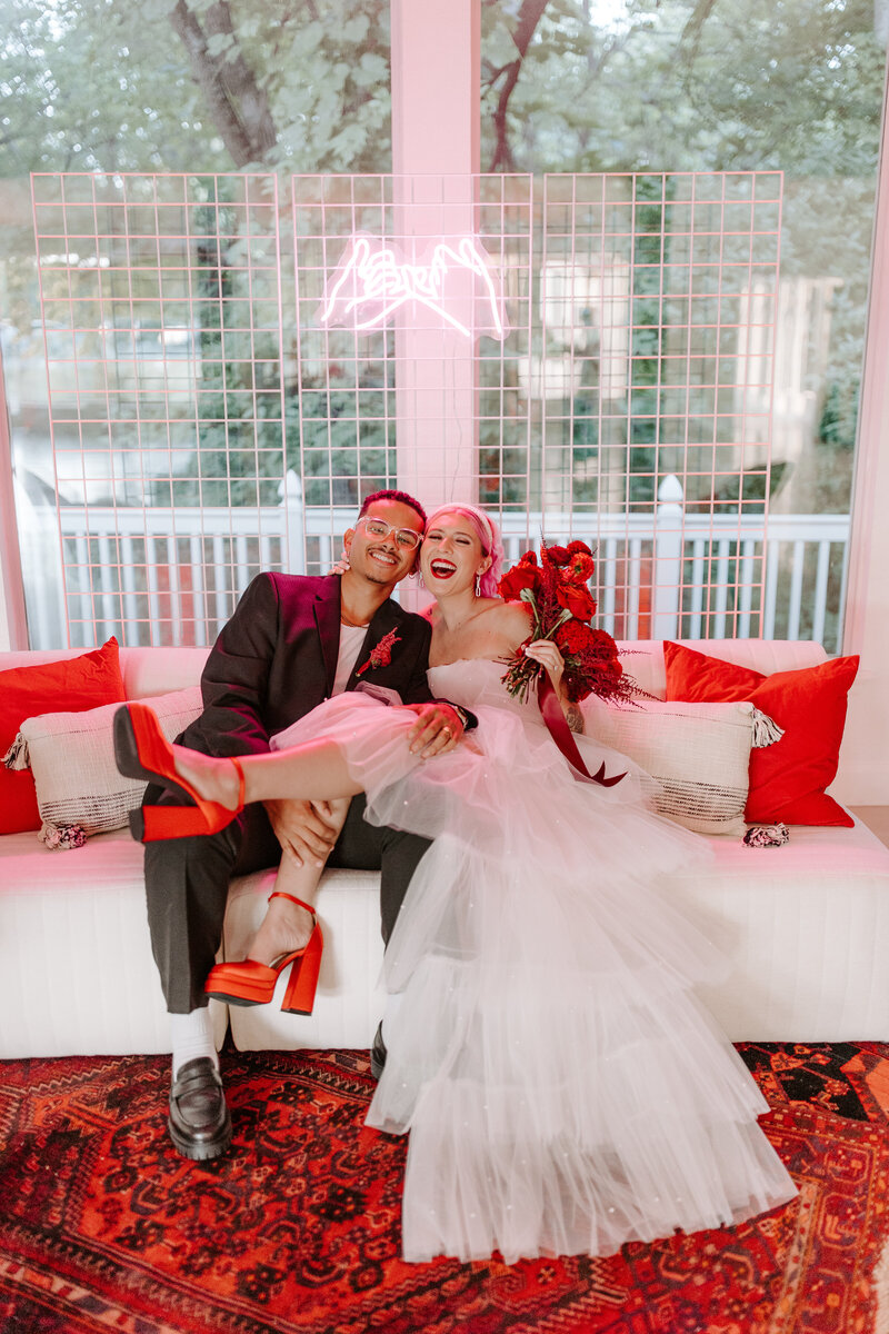 Bride and Groom sitting on a white couch with red accent pillows
