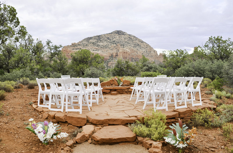 Sedona elopement ceremony with white chairs and flowers setup on red rocks patio backyard with mountain background