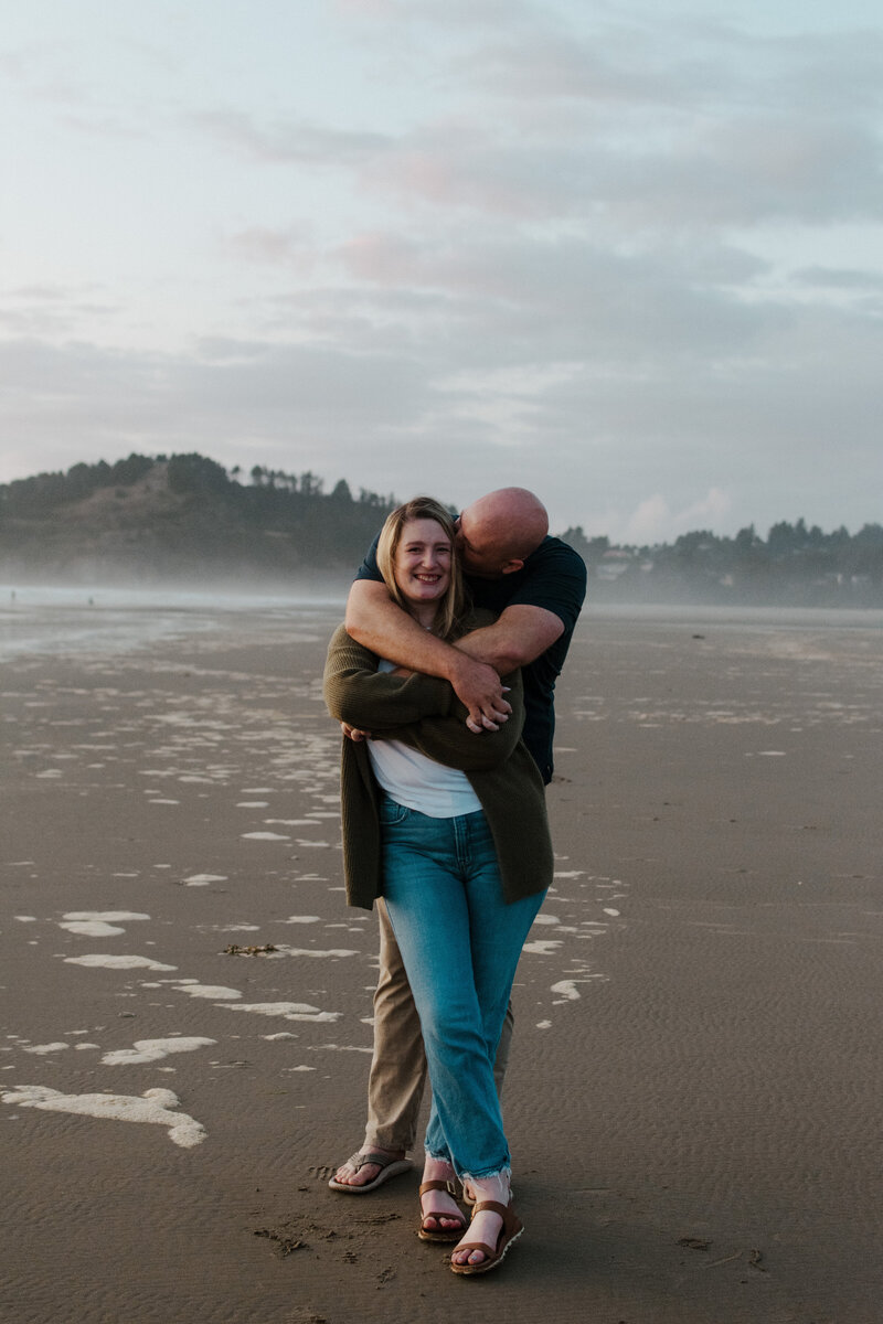 Couple standing on the Oregon Coast wrapped up in each other.