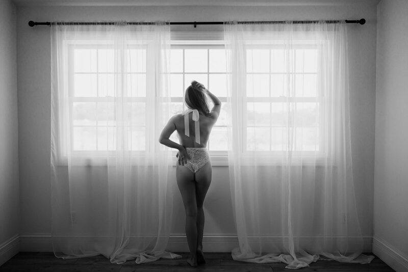 Woman in lingerie looking out the window and holding her hair up with one hand