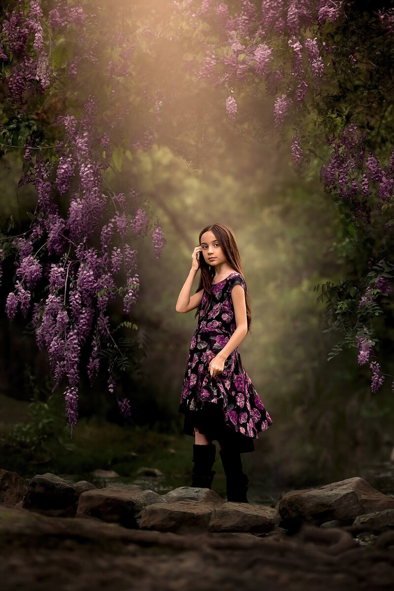 Beautiful brown haired girl posing close to a Wisteria tree wearing a dress that matches her surroundings.