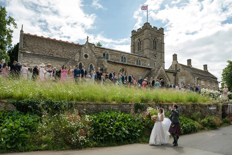 Scenic shot of church with guests lining path as they wave off couple