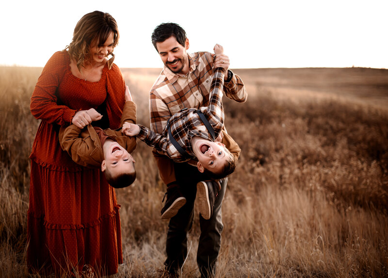 mother and father each holding a son and dipping him back toward the camera in a Wyoming field in fall.